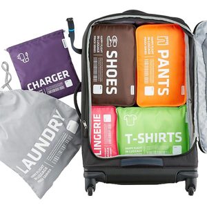 Suitcase contains labeled packing cubes for shoes, pants, lingerie, and T-shirts. Nearby, labeled bags for chargers and laundry are visible.