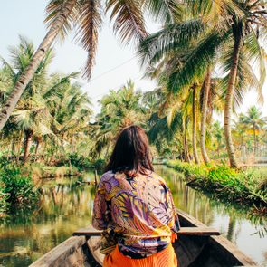 Person sits in a canoe, traversing a lush, palm-lined river under clear skies.