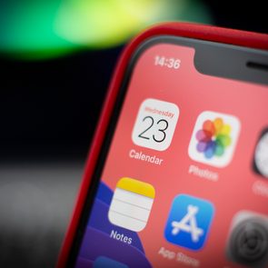 Close-up of a smartphone screen displaying app icons with a visible red case in a blurred background.