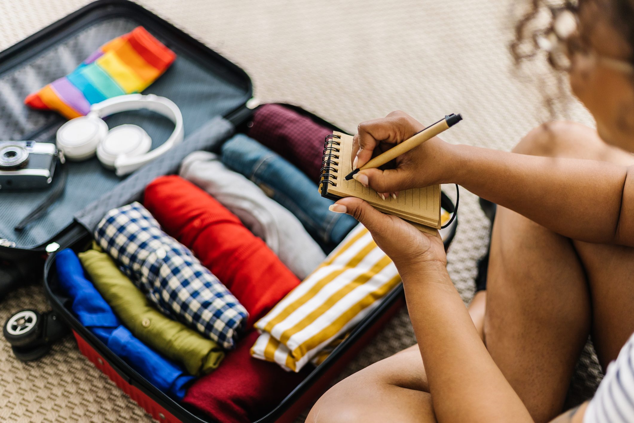 Mixed race young adult woman writing list of accessories and travel stuff before going on summer holidays