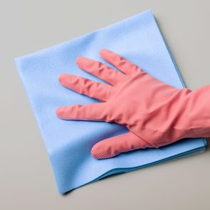 Gloved hand wipes a blue cloth on a smooth, light gray surface.
