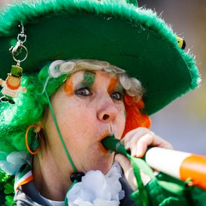 Woman blowing horn, dressed in festive green attire, with a large hat and matching face paint, amidst outdoor celebrations. Keychain reads 