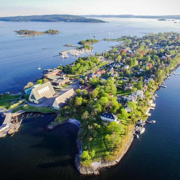 Coastal town spreads along a peninsula, surrounded by calm blue waters, with lush green trees and small buildings lining the shoreline.