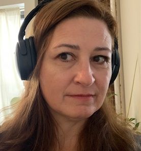 A person wearing black headphones looks ahead in a room with a light curtain in the background.