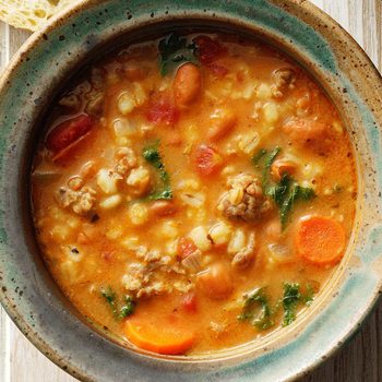 Hearty soup filled with vegetables, sausage, and grains in a ceramic bowl on a wooden table, creating a rustic and cozy setting.