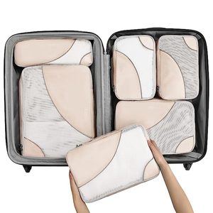 Packing cubes arranged in a suitcase, with hands placing one cube inside. Bags are beige with white mesh and gray accents.