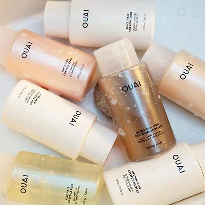Bottles of various Ouai hair products lie scattered on a white surface, each uniquely colored and labeled for specific hair care purposes.