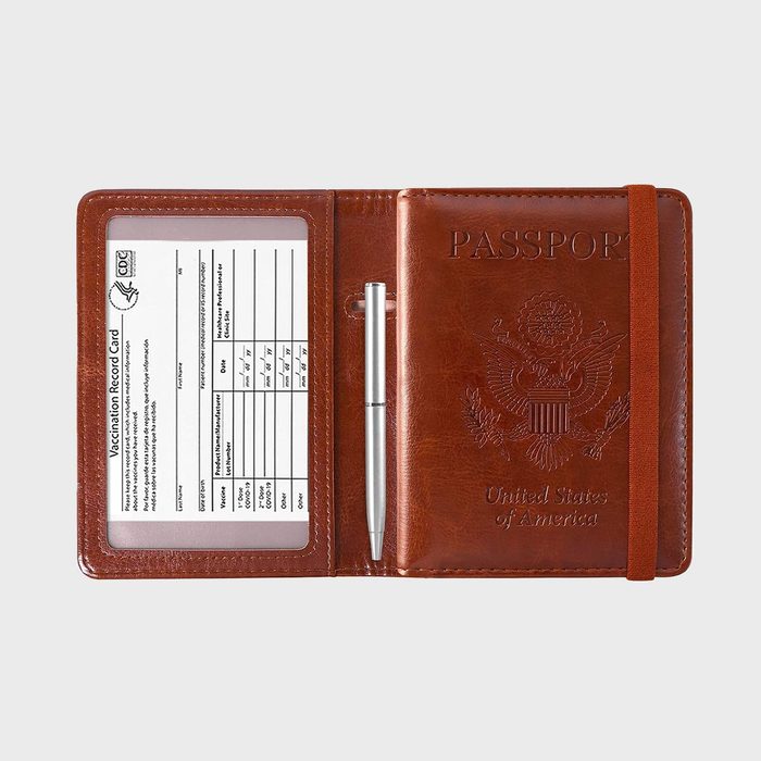 Passport holder displays a vaccination card and silver pen; brown leather with embossed U.S. emblem, arranged against a plain background.