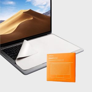 A laptop shows sand dunes, covered by a partially lifted white cloth, next to an orange GhostBlanket cleaning cloth package.