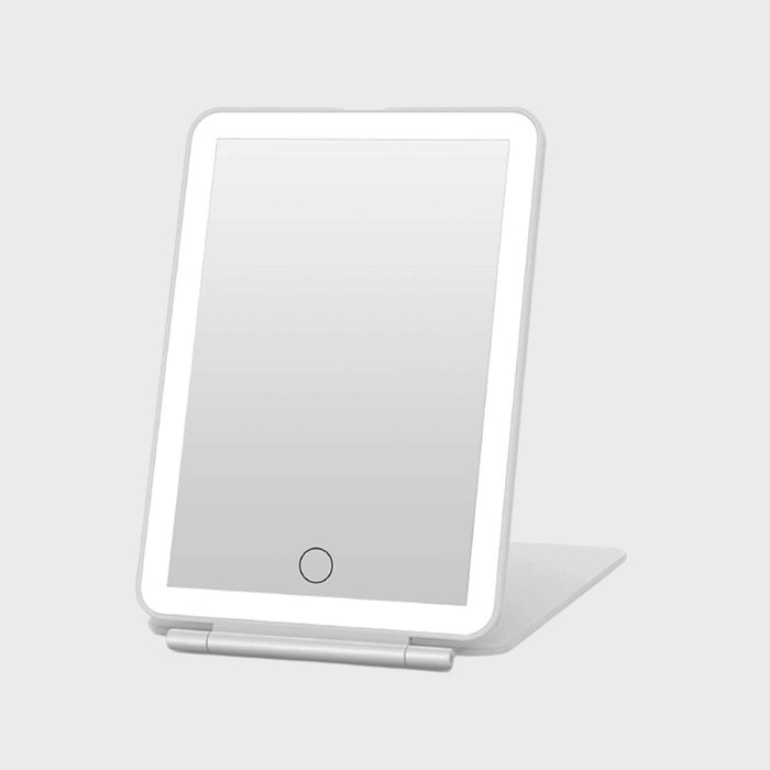 A rectangular mirror rests on a stand, featuring a circular touch button, set against a plain, light gray background.