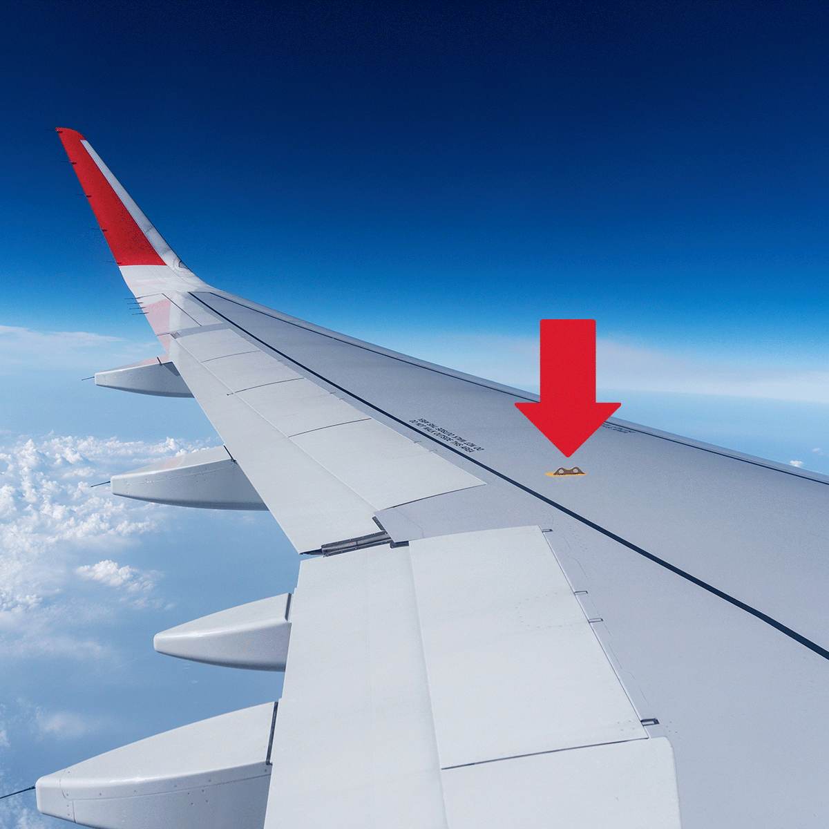 Airplane wing cutting through sky with red arrow pointing to small marking. Fluffy clouds spread across blue horizon below.