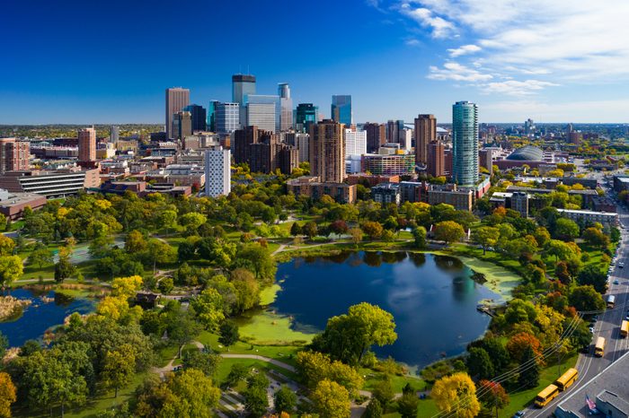 Skyscrapers stand tall under a clear blue sky, surrounded by a lush green park with a reflective pond, creating a vibrant urban oasis.