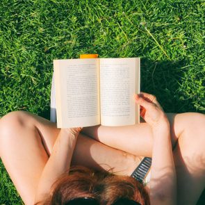 An open book is being read by a person sitting cross-legged on green grass outside.