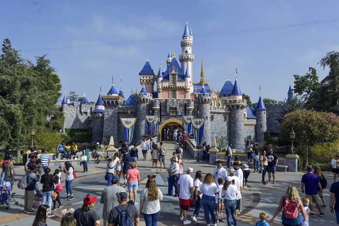 Castle stands gracefully while people gather and walk around; surrounded by trees and a clear sky.