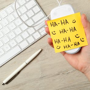 Hand holds a white computer mouse with a yellow sticky note reading 