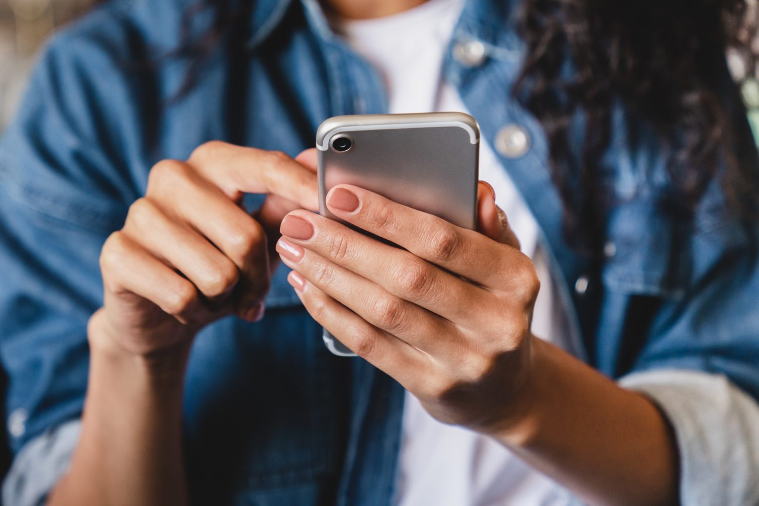 Cropped shot of an african-american young woman using smart phone at home. Smiling african american woman using smartphone at home, messaging or browsing social networks while relaxing on couch