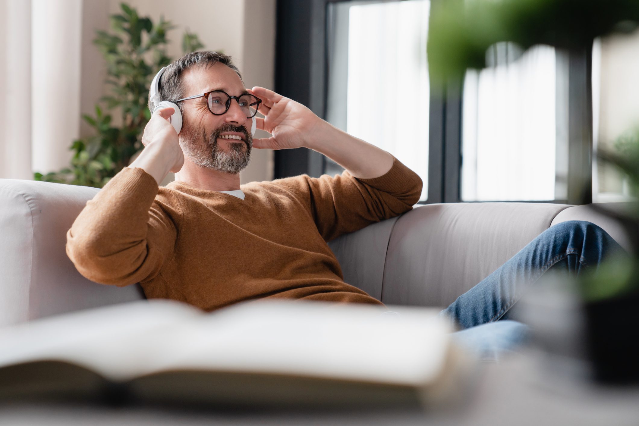 Chilling relaxed mature man father husband listening to the music in headphones lying on the sofa, enjoying sound tracks remotely. Break from working from home.
