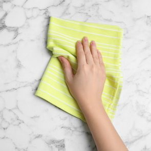 Hand wipes a marble surface with a yellow striped cloth.