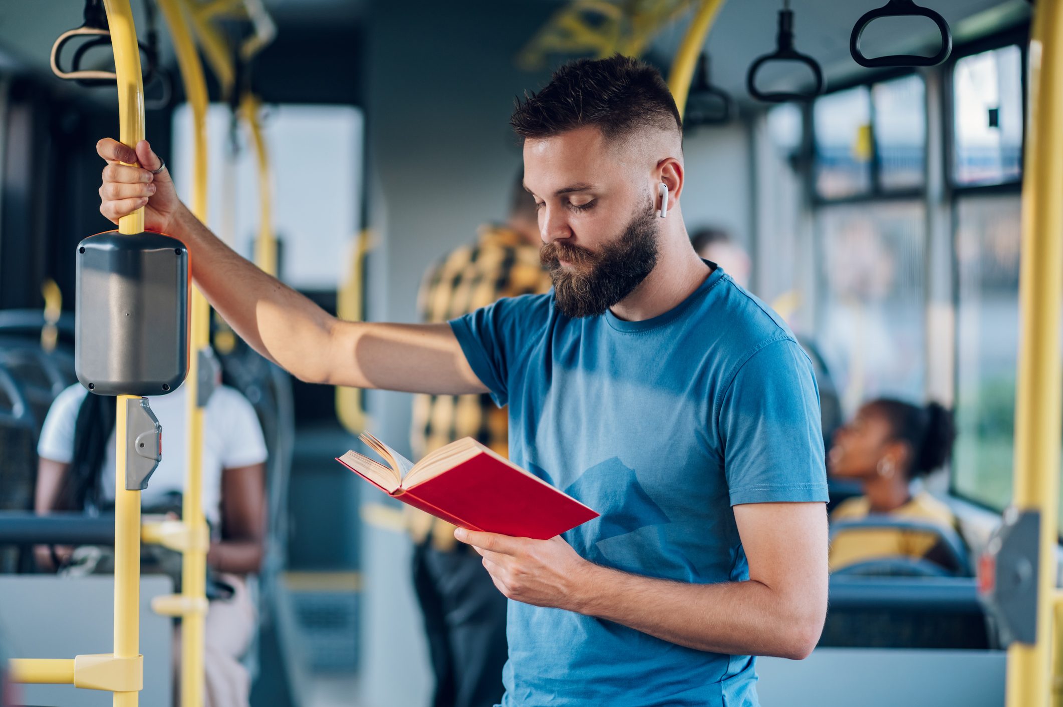 Man is riding in a bus and reading a book while holding for a bar