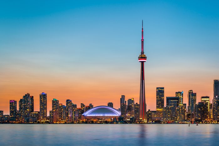 Tower illuminated in evening, set against a vibrant skyline with colorful sunset and water in foreground.