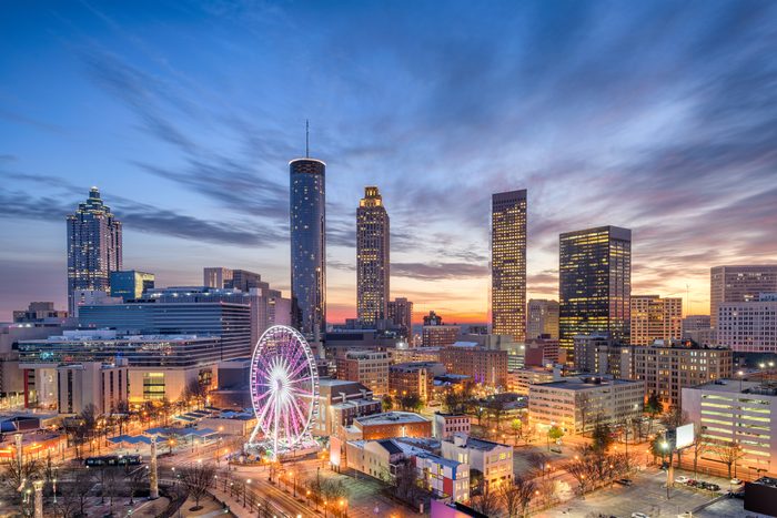 A Ferris wheel glows amid skyscrapers during sunset, casting colorful lights over the bustling cityscape with a vibrant sky.