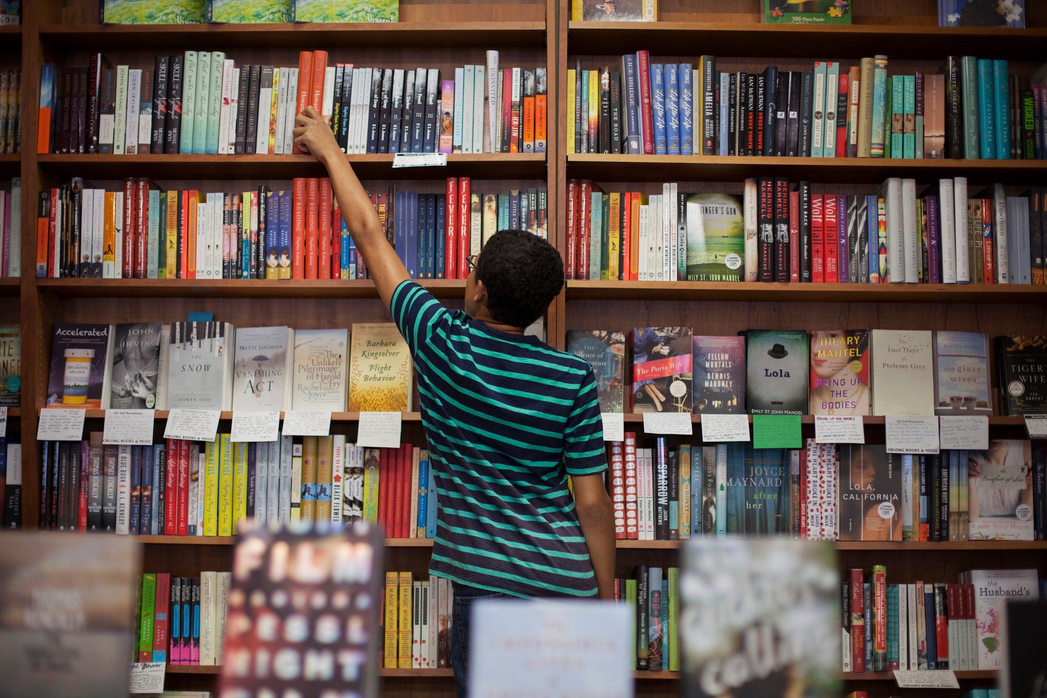 Rear view of man removing book from shelf while standing in store