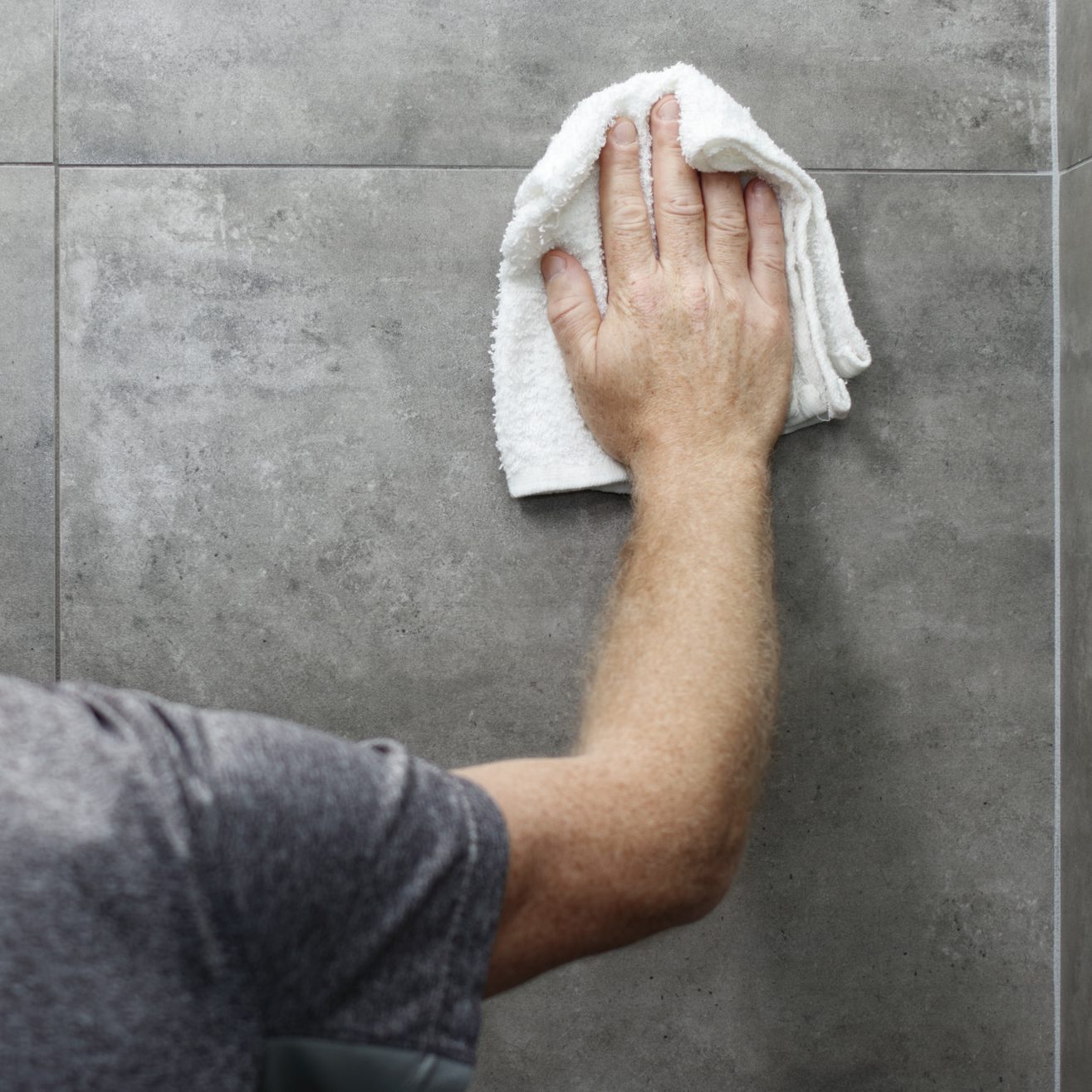 Guy Cleaning a Gray Tile Bathroom Shower Wall with a Rag