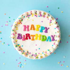 Cake displays â€œHAPPY BIRTHDAYâ€ in colorful letters, surrounded by sprinkles, against a light blue background.