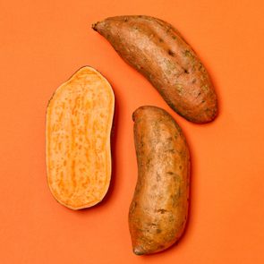 Three sweet potatoes, one sliced open showing orange flesh, rest on a bright orange background.
