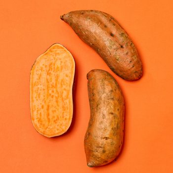 Three sweet potatoes, one sliced open showing orange flesh, rest on a bright orange background.
