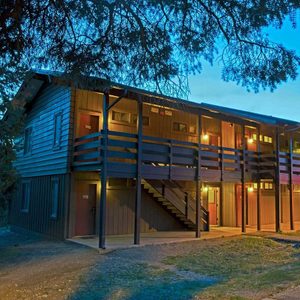Wooden building, illuminated, stands outdoors with stairs and balconies, surrounded by trees at twilight.