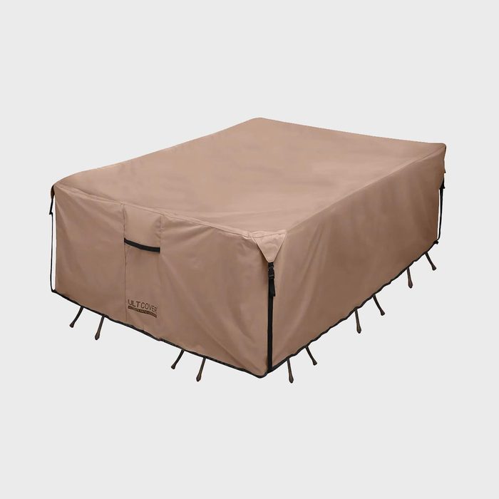 Tan protective cover encloses an outdoor table, secured with straps, on a plain white background. Text reads: 