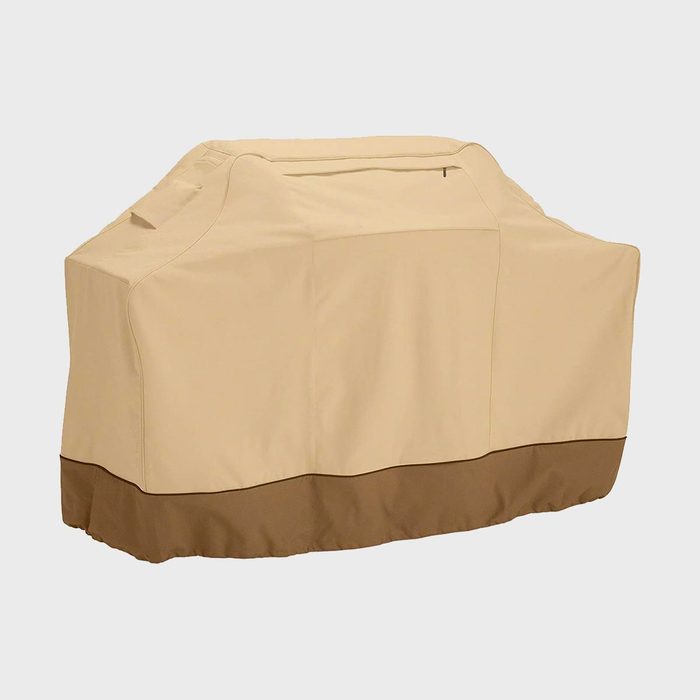 A beige grill cover drapes over a large outdoor grill, set against a plain white background.