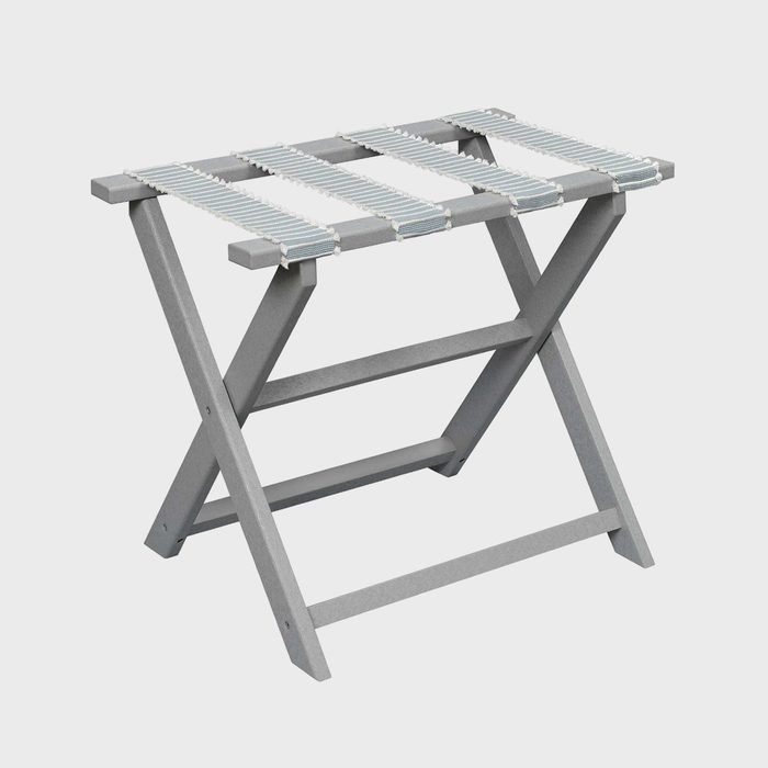 A gray luggage rack stands alone, featuring crossed legs and parallel fabric straps, on a plain white background.