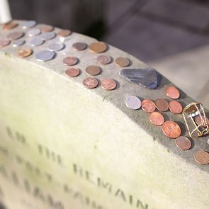 Coins and small objects rest on a tombstone amid a graveyard setting.