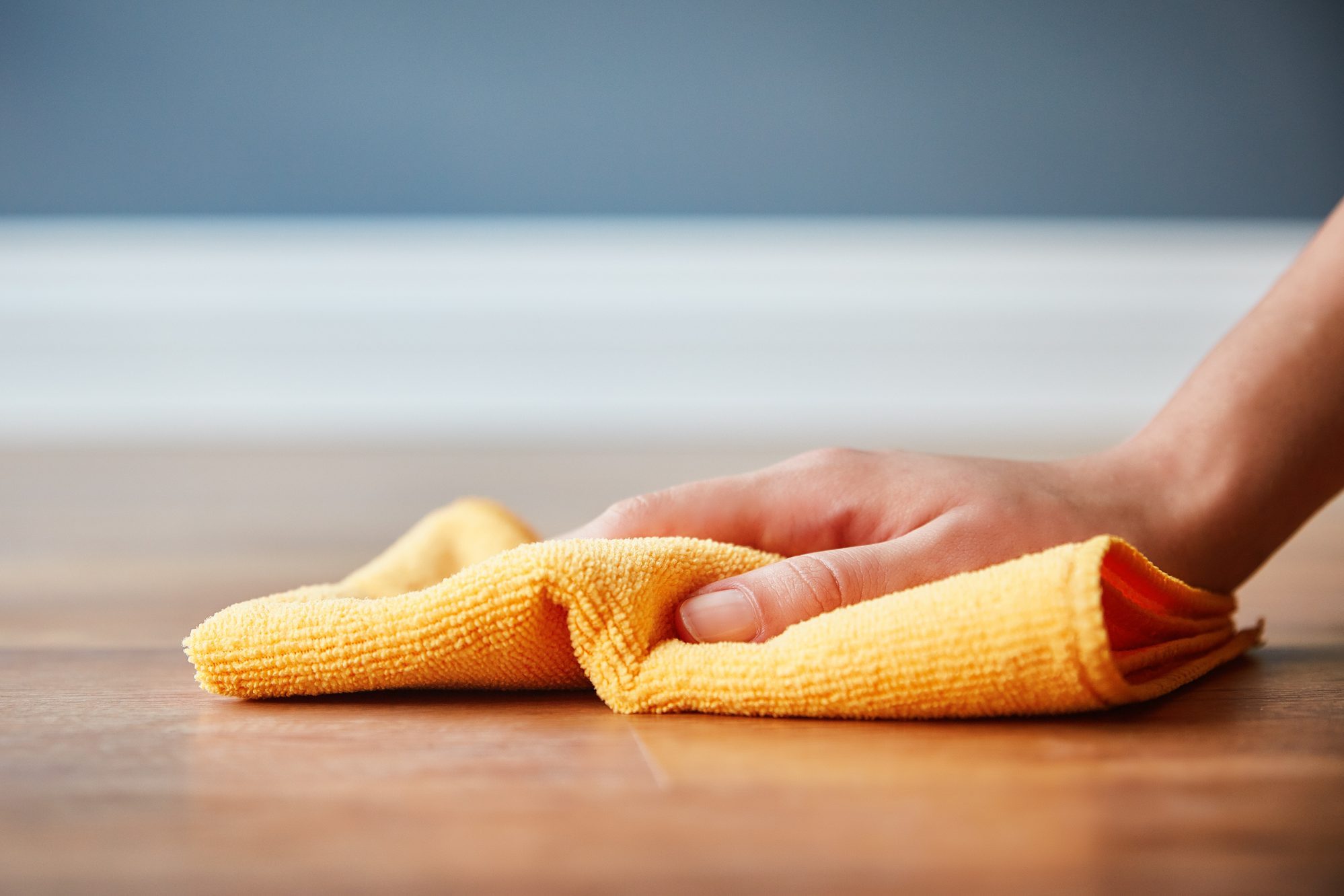 hand using mircrofiber cloth to clean the area of the floor close to the wall and baseboard