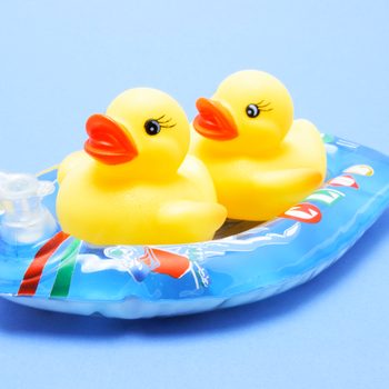 Two yellow rubber ducks sit on a colorful inflatable raft against a blue background.