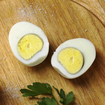 Halved boiled eggs rest on a wooden cutting board, sprinkled with coarse salt and garnished with fresh parsley leaves.