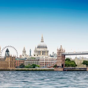 Famous landmarks tower over a river, under a clear blue sky, blending historic and modern architectural styles in a cityscape.