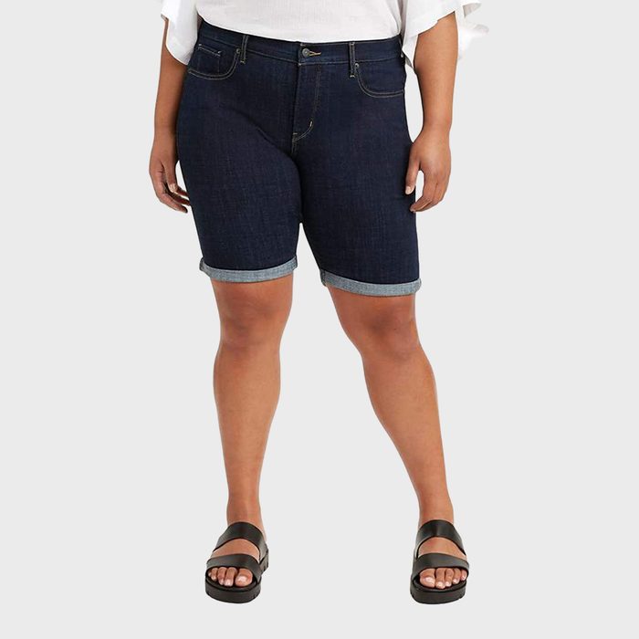 Person wearing dark denim shorts, standing with hands relaxed in a neutral pose against a plain, light background.