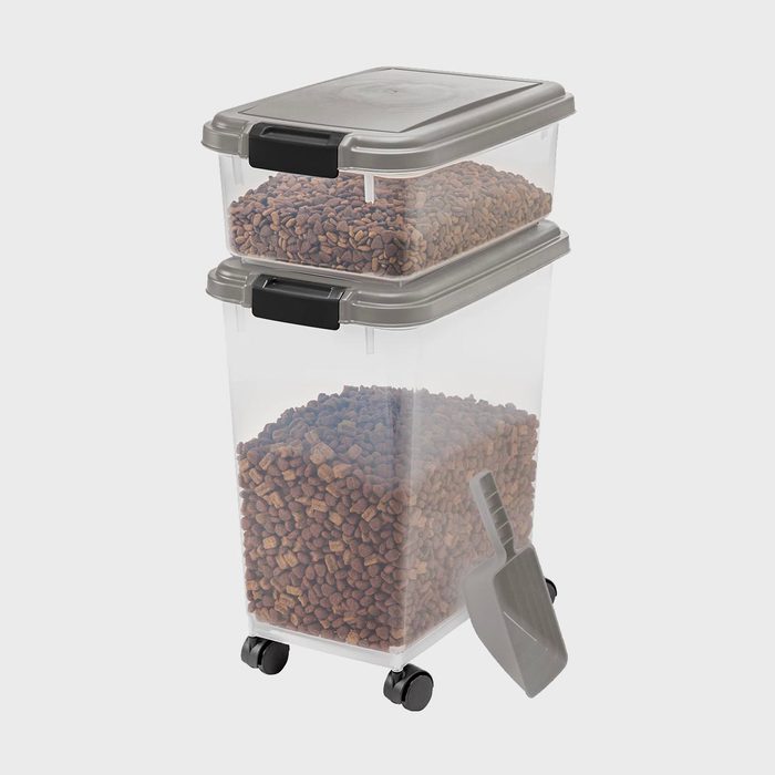 Transparent containers hold pet food, stacked on top of each other with grey lids, alongside a scoop; situated on a plain background.