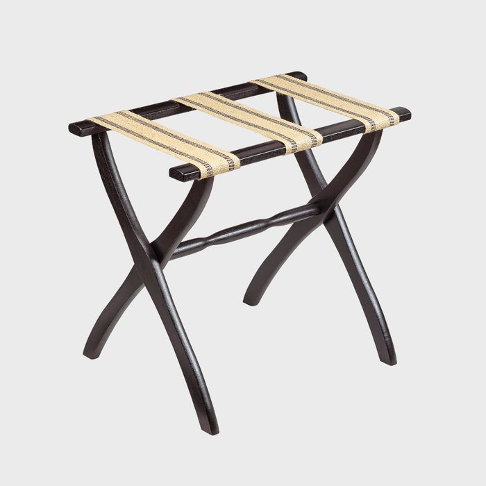 A luggage rack with wooden legs unfolds, featuring tan fabric straps, set against a plain white background.