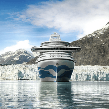 A large cruise ship sails toward a glacier, surrounded by mountains under a clear blue sky.