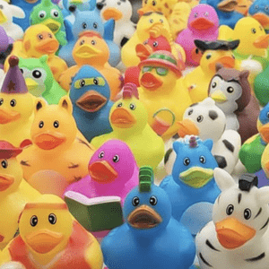 Colorful rubber ducks, varying in costumes, stand together in a crowded arrangement. They are adorned with different accessories, creating a playful, diverse display.