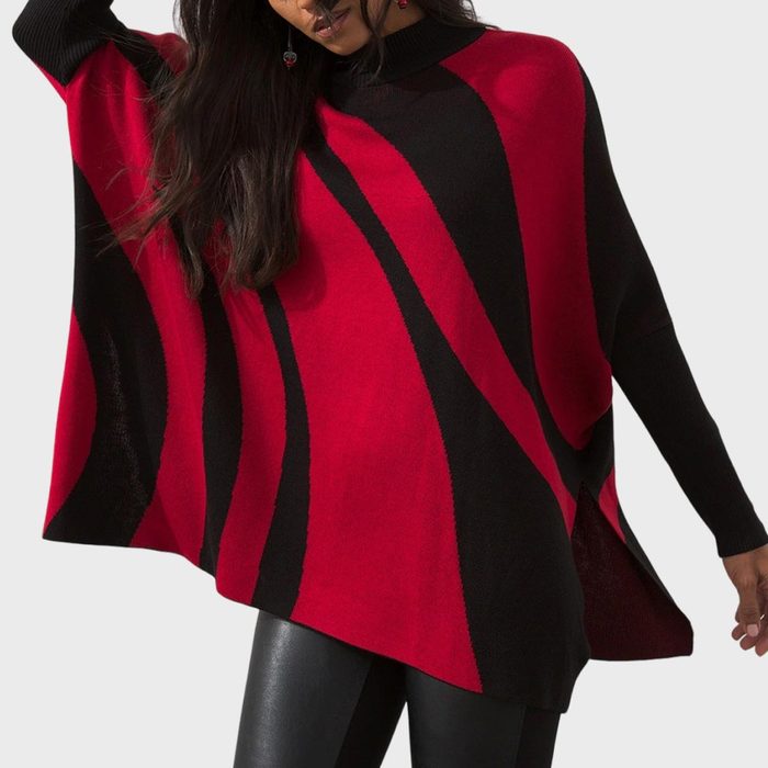 A person wears a red and black striped poncho, holding it out slightly, standing against a plain, light background.
