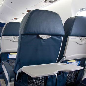 Airplane seats face forward, tray tables are open, and windows let in light in an empty cabin.