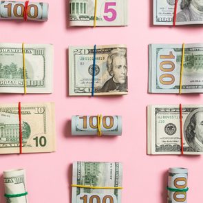 Bundles of U.S. currency wrapped with rubber bands are arranged on a pink background.
