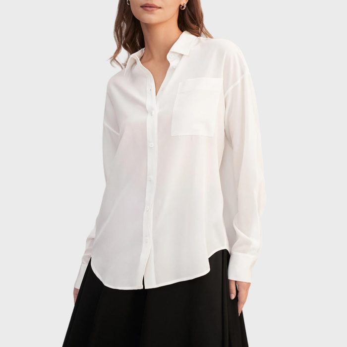 A person wearing a white button-up shirt with long sleeves, featuring a pocket, standing against a plain gray background.