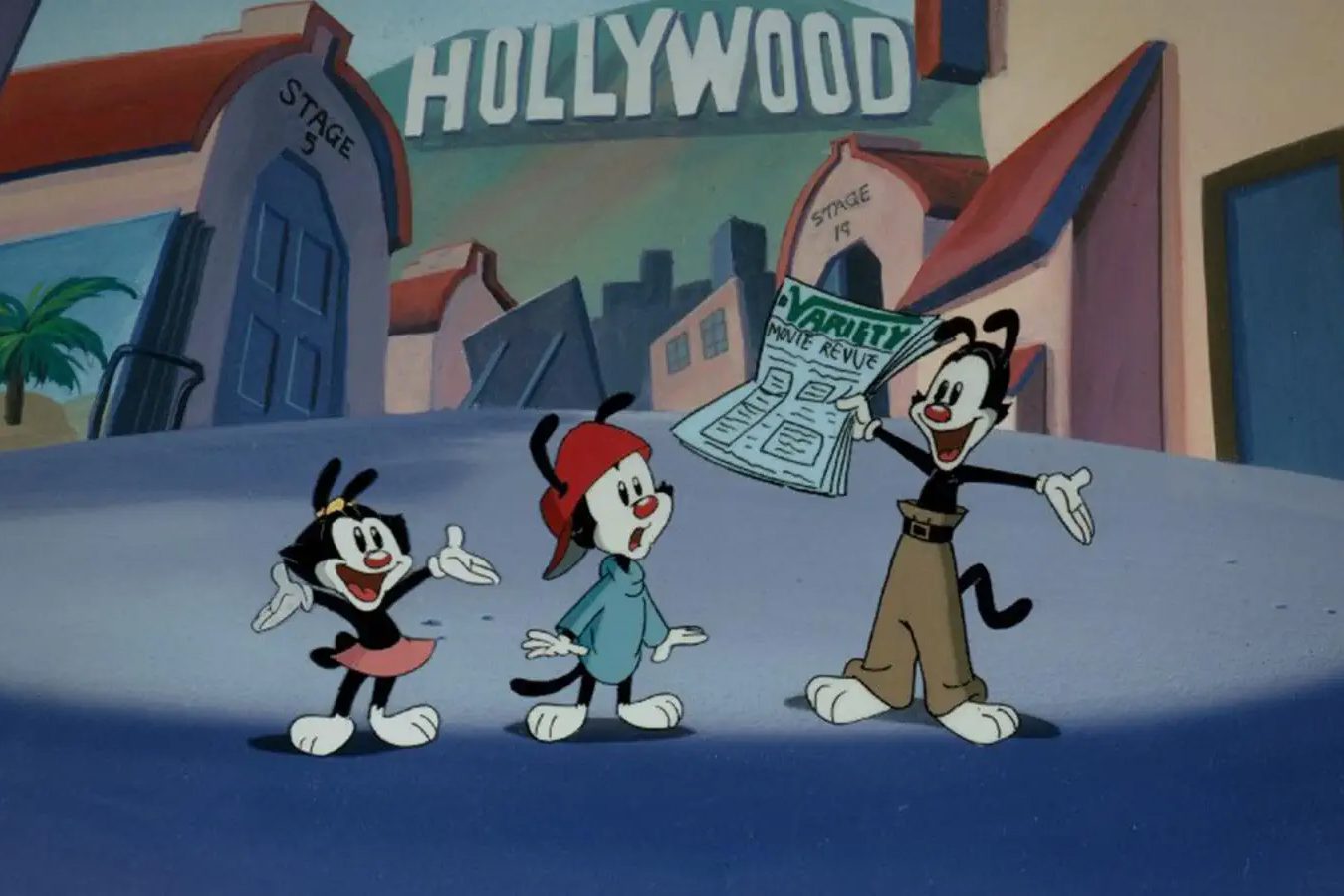 Three cartoon characters excitedly react to a newspaper outside a Hollywood studio. Signs read "HOLLYWOOD," â€œSTAGE 5,â€ and â€œSTAGE 14.â€