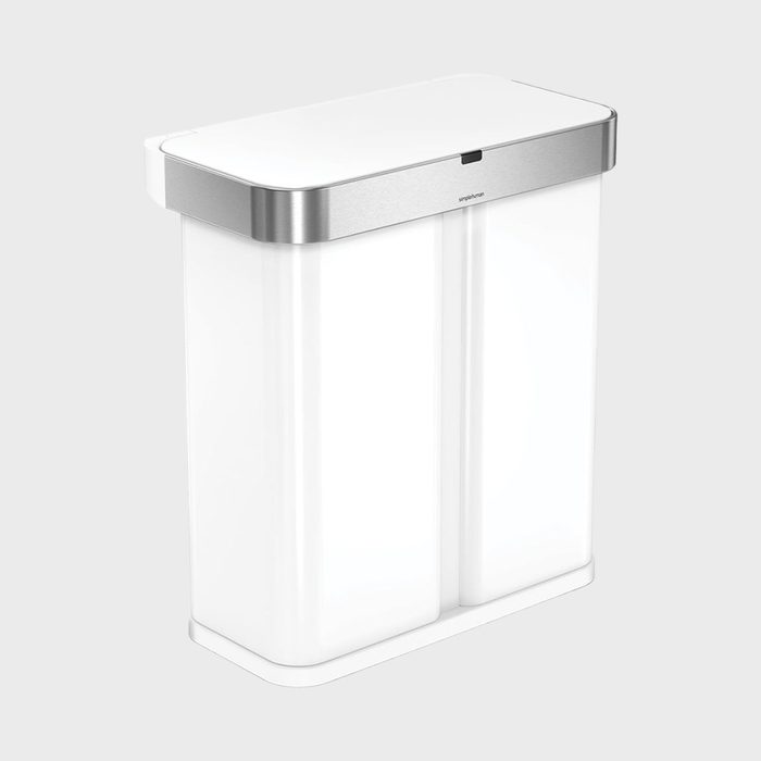 A dual-compartment trash can, standing upright, with a sleek, stainless steel top in a minimalist setting.